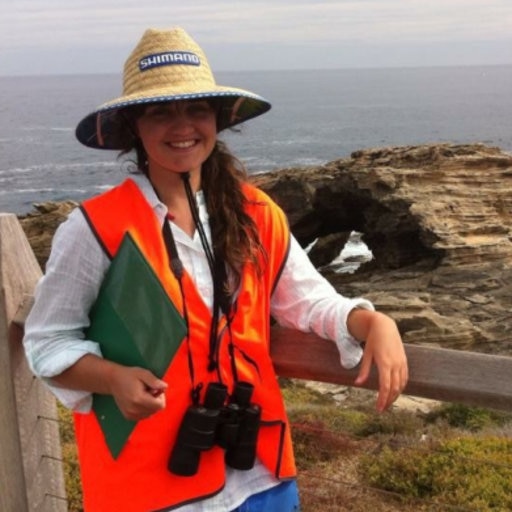 Woman in hi-vis vest stands with coastline in the background