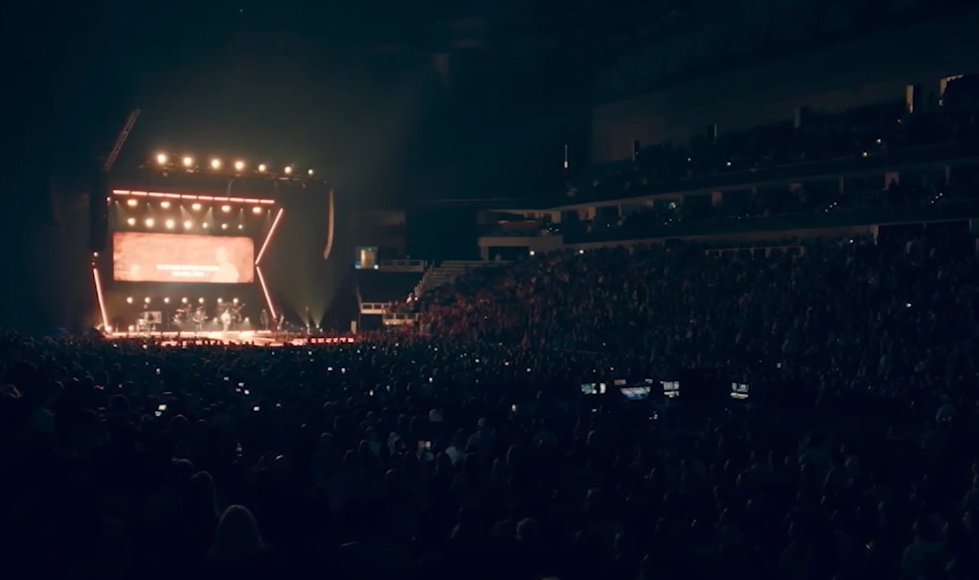 Uma multidão no escuro com um grande palco iluminado.