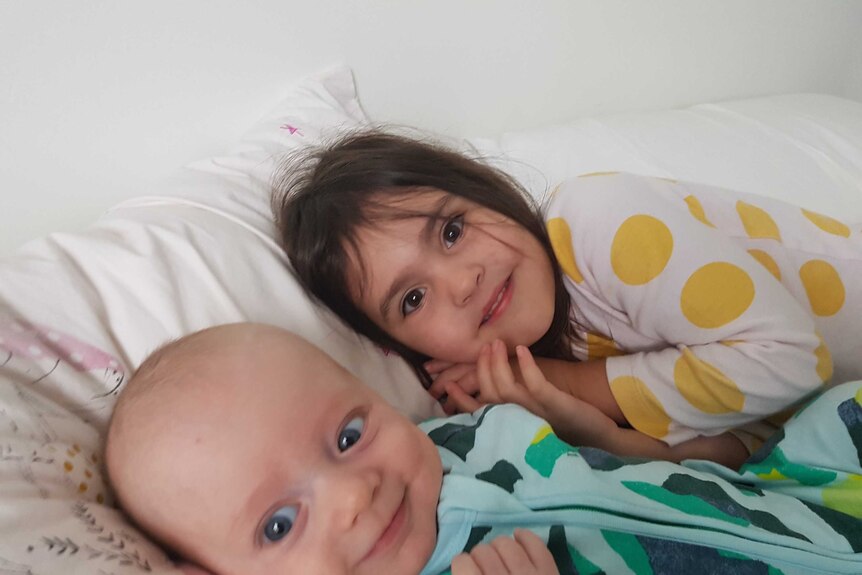 A baby boy and his big sister lie in bed in their pyjamas