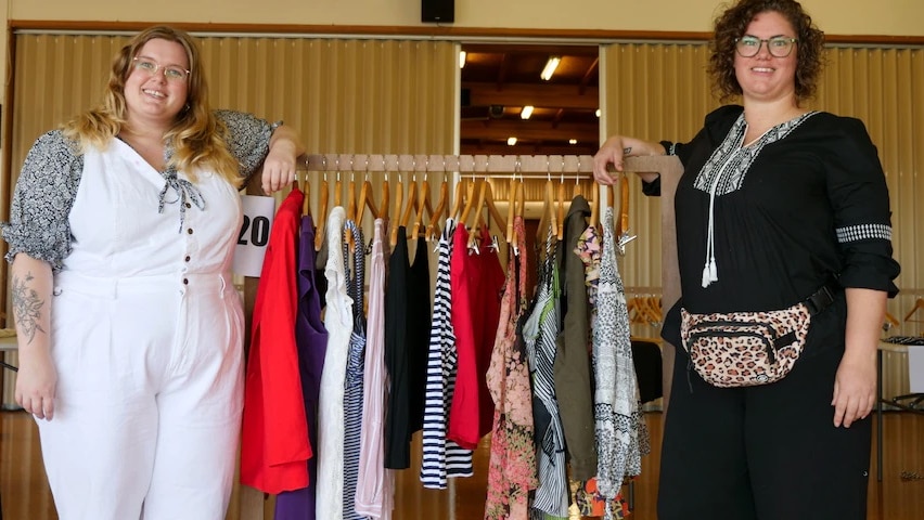 Two women, Katie Parrott and Bonnie Tuttle, stand next to a clothes rack of size 20 clothing.