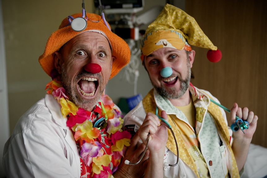 The two clowns smile broadly, wearing costumes, with colourful noses and hats.