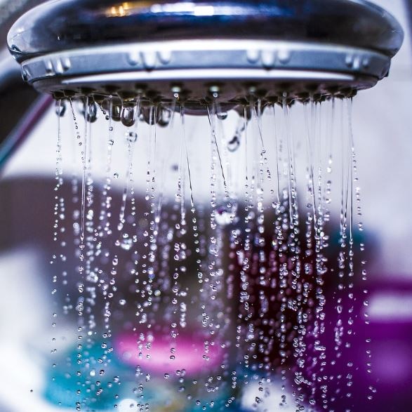 Photo of a shower head with water dripping out of it.  There are blue and purple type colours in the background