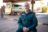 Paramedic sits in car park with ambulance in background 