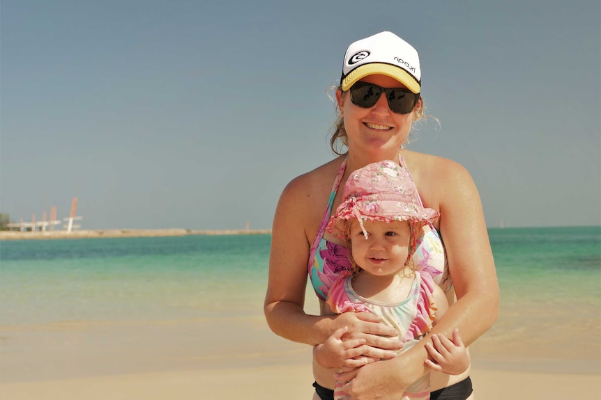 A mum holds her baby at the beach.