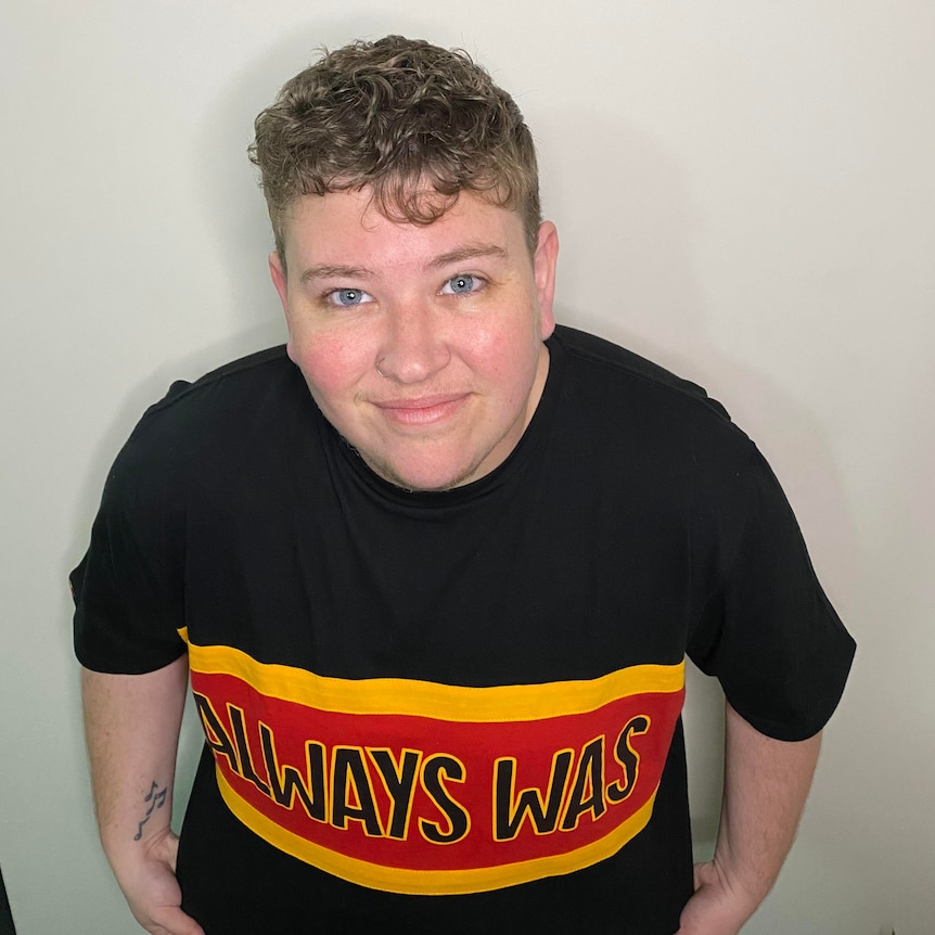 Photo of Stevie looking at the camera wearing a black shirt with red and yellow panel that reads "always was, always will be"