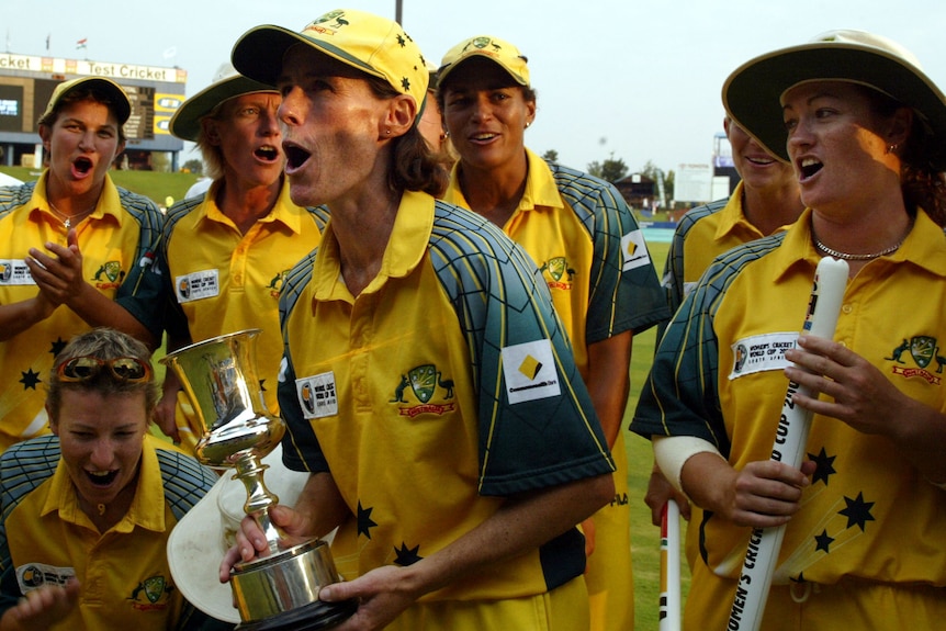 Belinda Clark holds a trophy and is surrounded by teammates celebrating