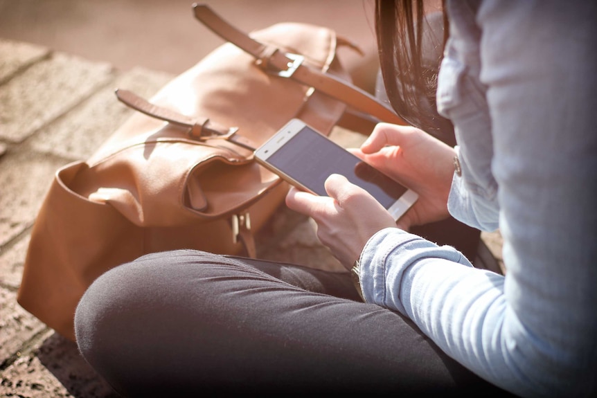 Woman sitting down holding phone with two hands