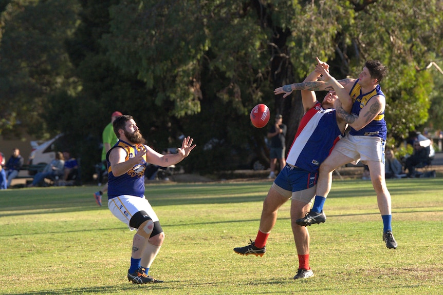 a footy player hits the ball out of the way as his opponent reaches up to grab it