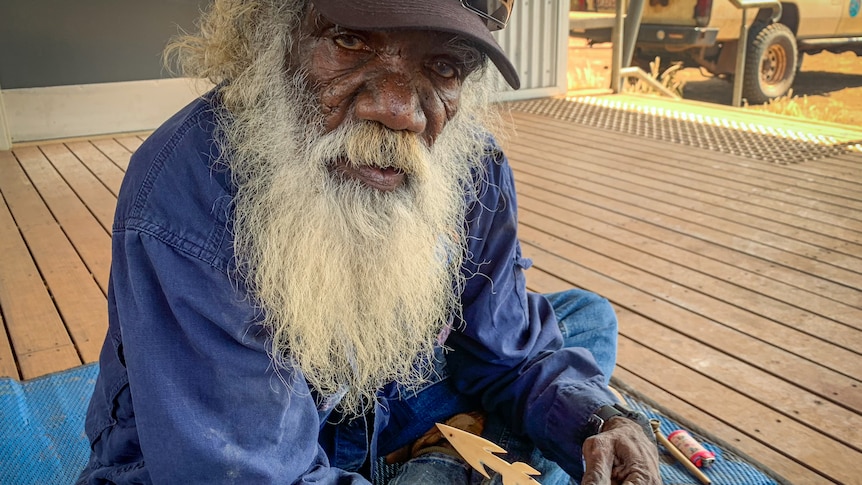 Dennis Maminyamanja making a traditional spear, sitting cross legged.