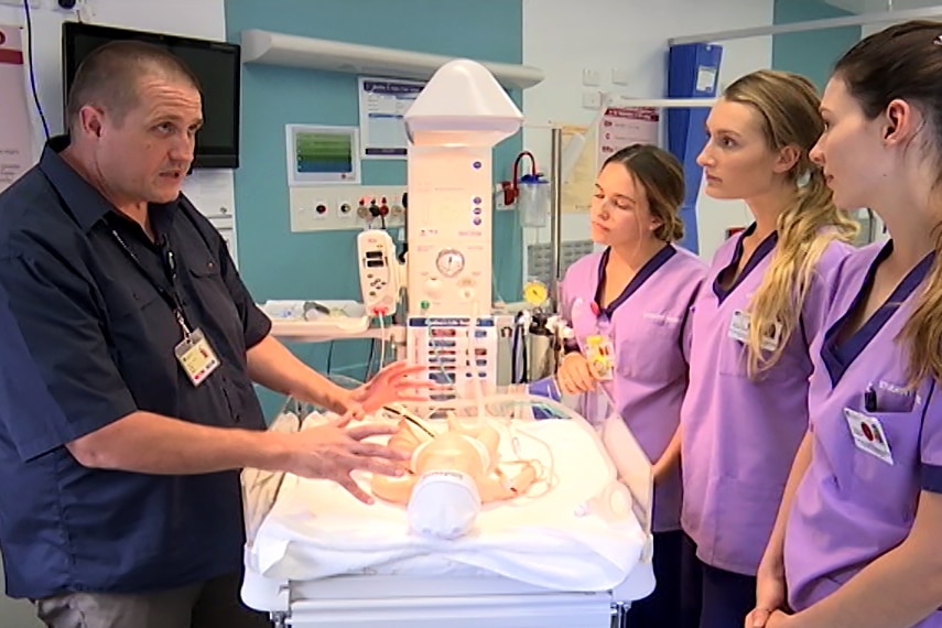 Male academic instructs three female students in a hospital room.