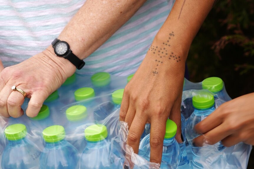 A close up image of two womens' hands holding bottles of water