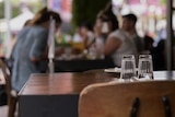 Glasses on a table at a restaurant with people enjoying food in the background.
