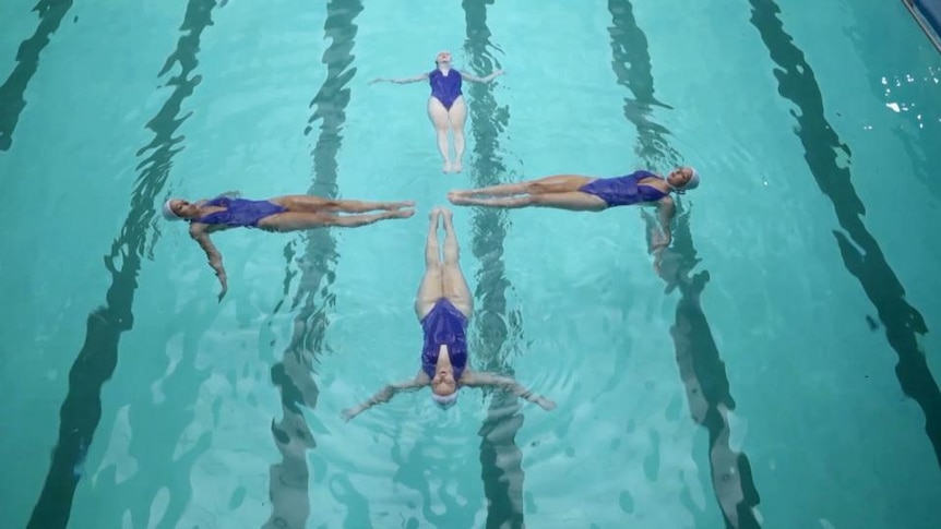 Four synchronised swimmers float on their backs in a cross formation with their feet towards the centre