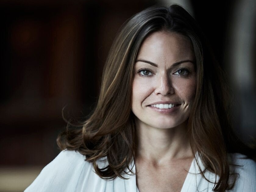 A woman with wearing a white blouse against a black background.