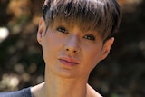 A tight head and shoulders shot of a woman with short hair wearing a black shirt and nose ring posing for a photo outdoors.