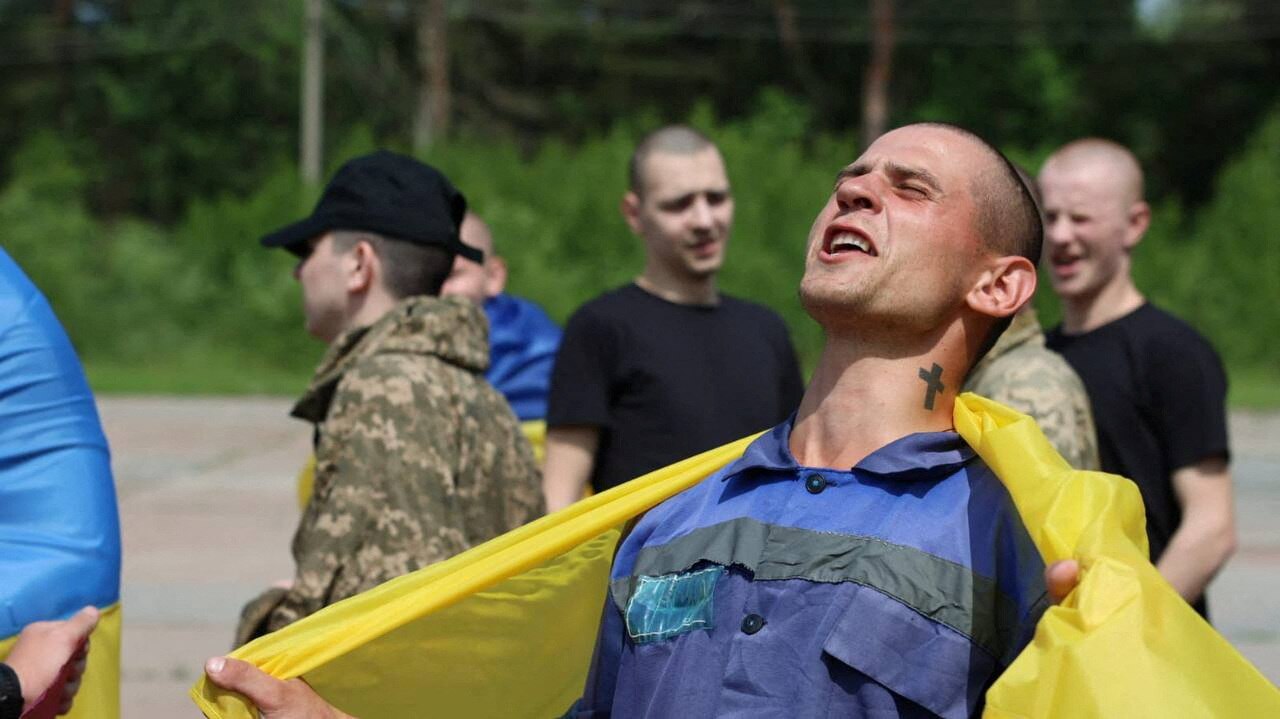 A man with a ukrainian flag wrapped around him holds his head back and cheers