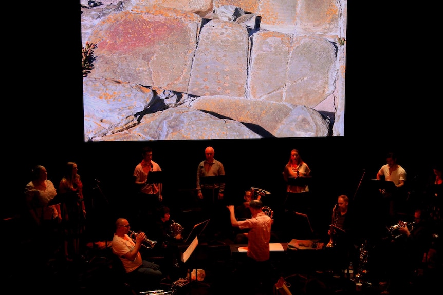 An orchestra rehearses in front of a projection of rocks