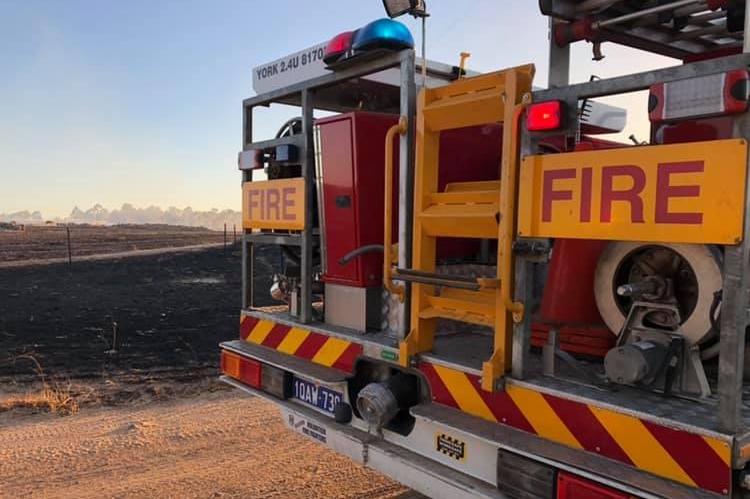 A fire engine parked on a bush track near a smouldering landscape.