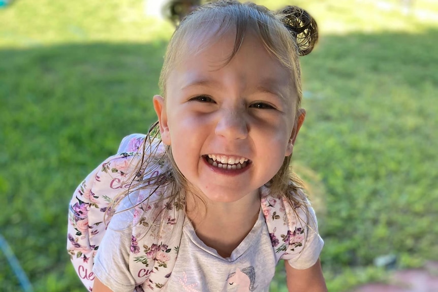 A young girl smiles while looking up towards the camera wearing a backpack.