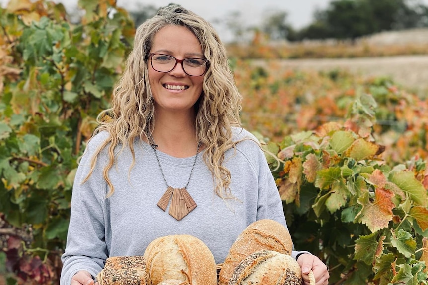 A lady stands in front of a vineyard with a basket of bread