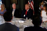Donald Trumps speaks with his arms folded while sitting at a table flanked by Melania Trump and Tom Price.