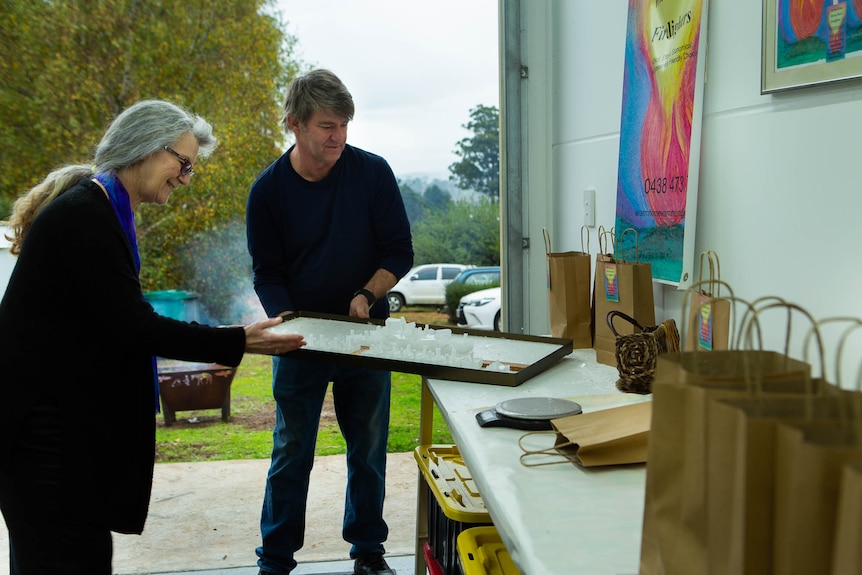 A couple carefully manouvre a tray towards a bench inside a garage.