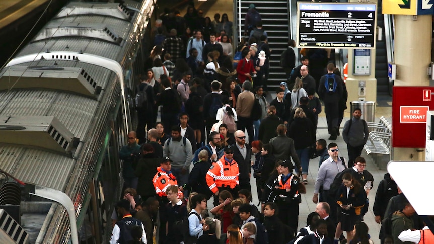 A crowd moves on and off a train at Perth Station from the Fremantle Line as transit guards stand by