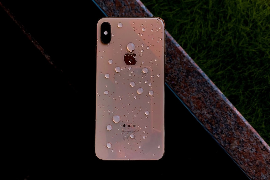 An iPhone face down with water droplets on the exterior.