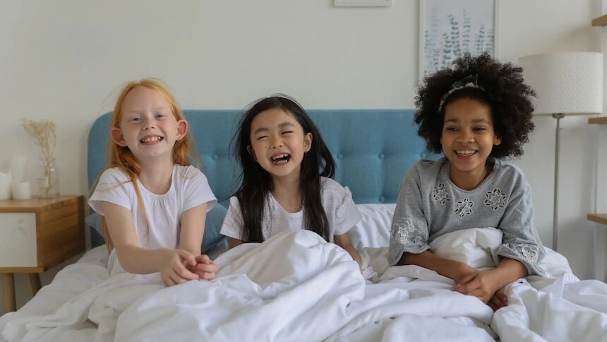 三个孩子坐在床上笑。