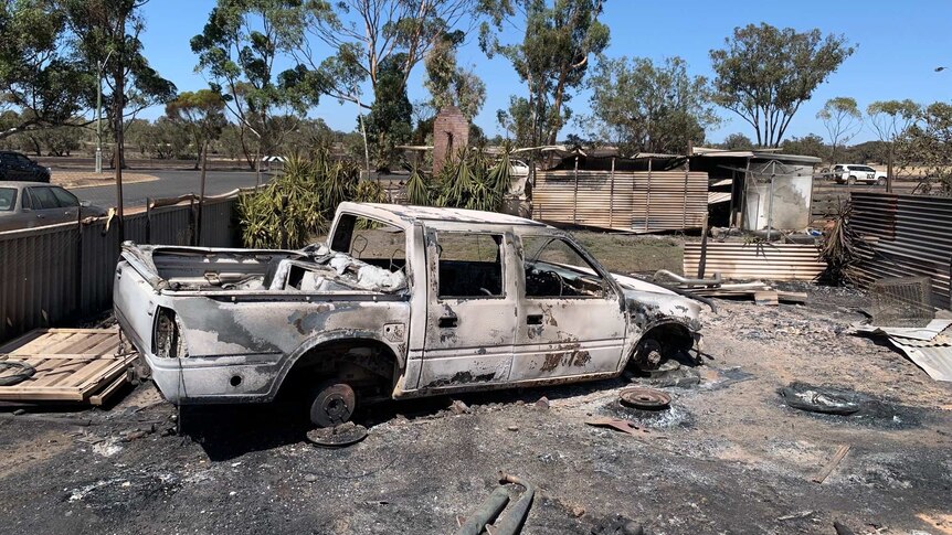 The body of a car torched by the fire sits in a yard surrounded by scorched corrugated tin.