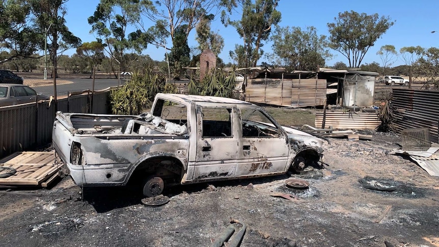 The body of a car torched by the fire sits in a yard surrounded by scorched corrugated tin.