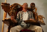 A man sitting on large wooden chair carved into the shape of a dragon.