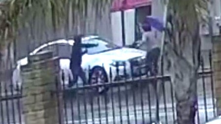 A picture taken from CCTV showing a man chasing a woman holding a purple umbrella around a car on the opposite side of the road.