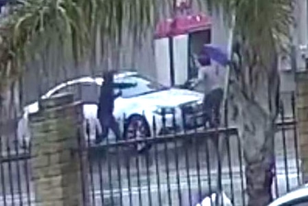 A picture taken from CCTV showing a man chasing a woman holding a purple umbrella around a car on the opposite side of the road.