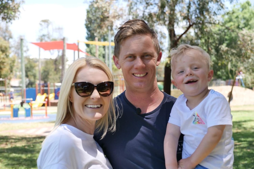 A mother, father and their son stand in a park.