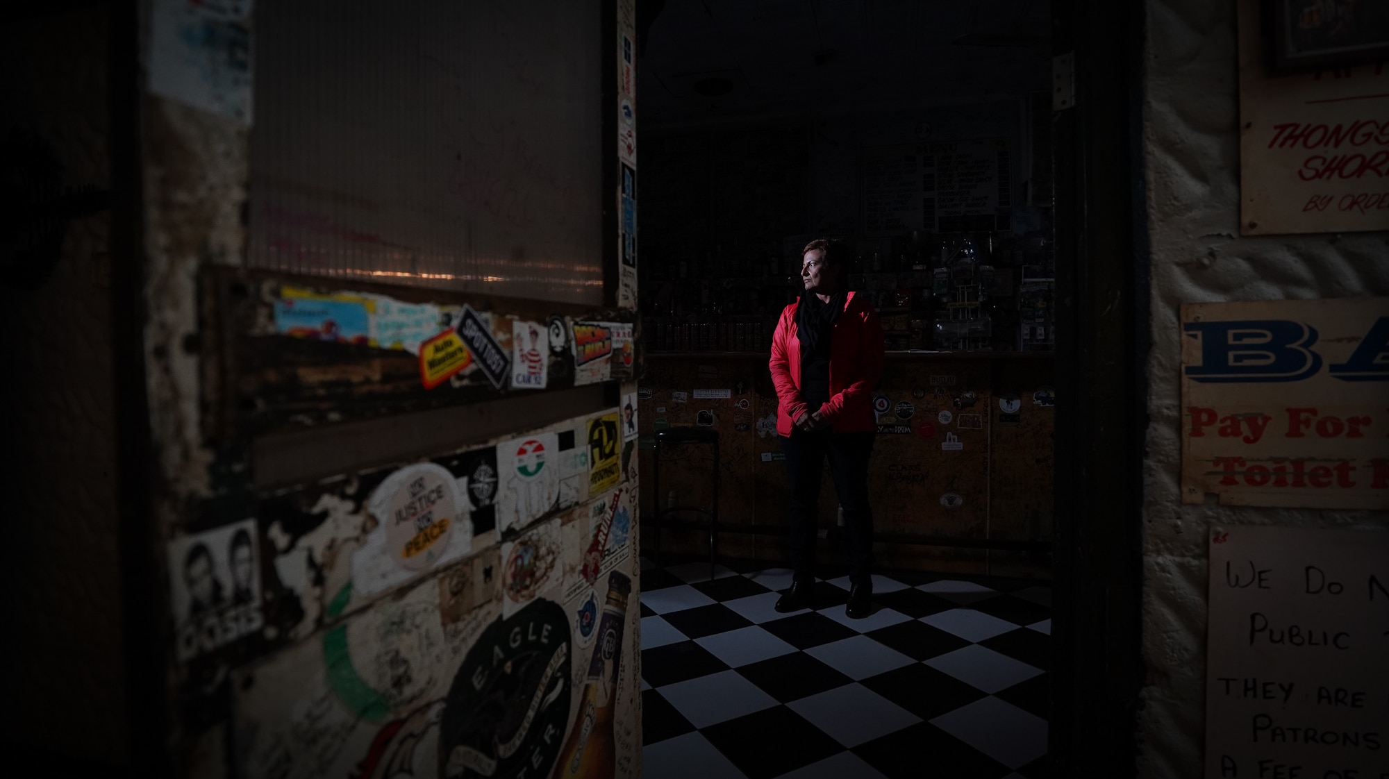 A wide shot taken through a hotel's front door shows a woman standing inside the pub, the photo is dark and eerie.