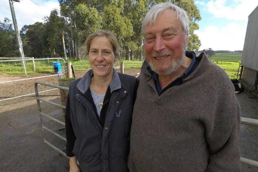Nicole and Rodney May stand near a rural shed with paddocks and stock yards behind them.