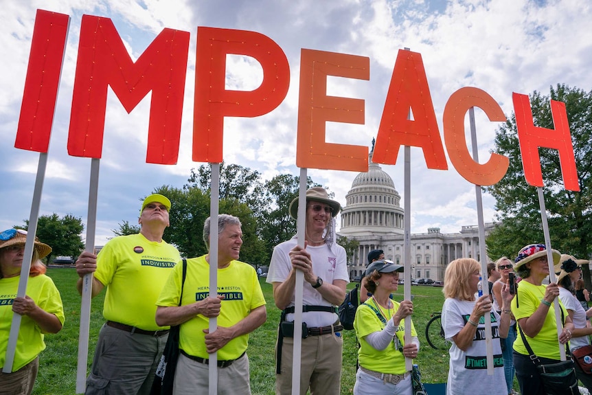 Aktywiści walczą o postawienie w stan oskarżenia prezydenta Donalda Trumpa, trzymając list ze słowem impeachment.