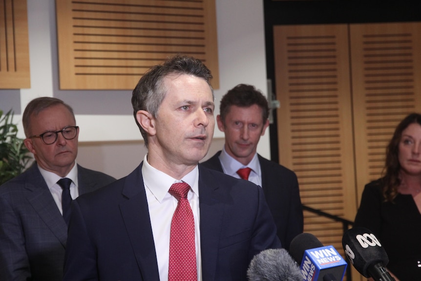 Man stands at podium with three  people behind him