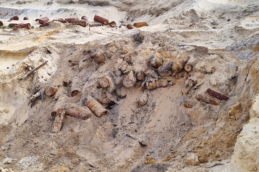 Rusty gas bottles stick out of sandy soil in an area likely exposed by a digger.