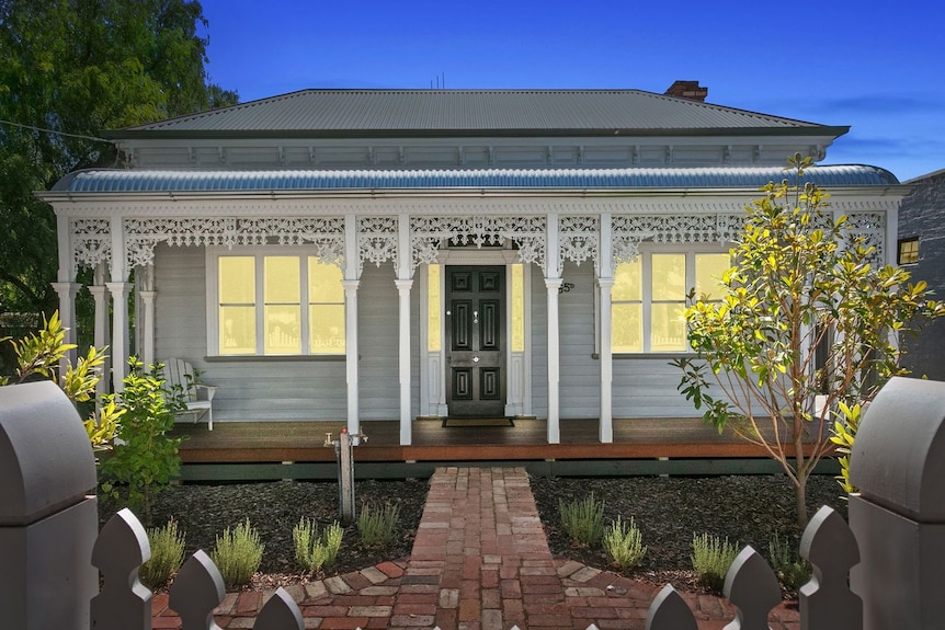 A verandah with decorated white pillars fronts a country home.