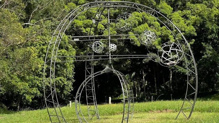 A metal art structure, featuring a round dome, sitting in a grass field.