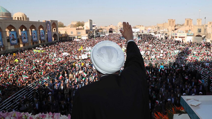 President Hassan Rouhani holds one hand high as he waves to a large crowd of people.