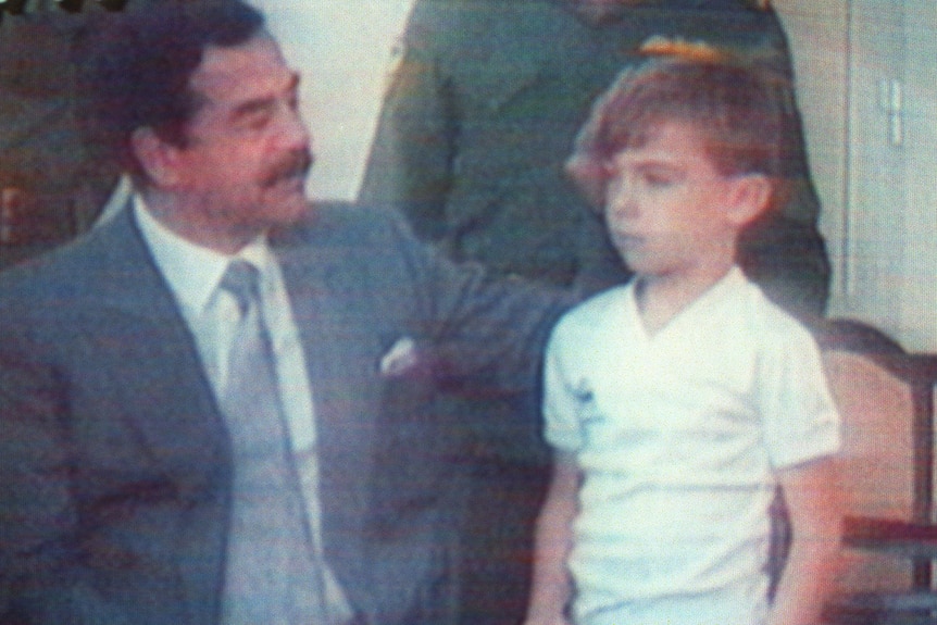 Saddam Hussein pats the head of a young boy.