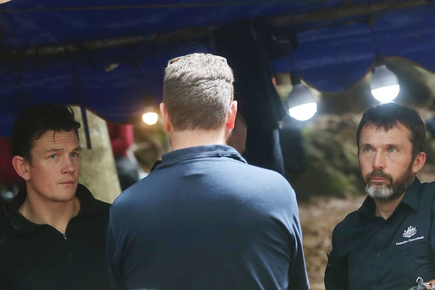 Two men from the AFP look at a third man with his back toward the camera, with serious expressions.