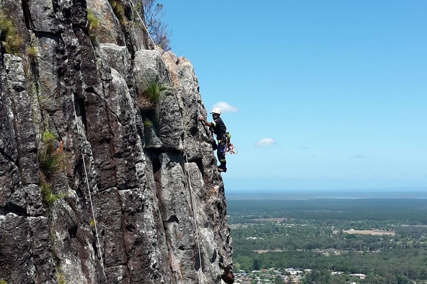 A QFES rescuer trains on a cliff on Mt Ngungun, one of the Glasshouse Mountains on the Sunshine Coast