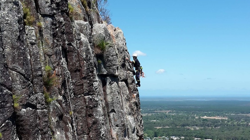 A QFES rescuer trains on a cliff on Mt Ngungun, one of the Glasshouse Mountains on the Sunshine Coast