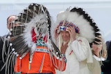 Pope Francis wears a traditional head dress and stands facing another person in traditional dress. 