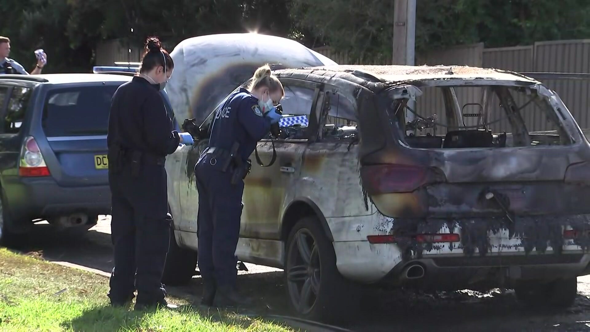 Forensic police officers take photographs of a burnt-out car. 