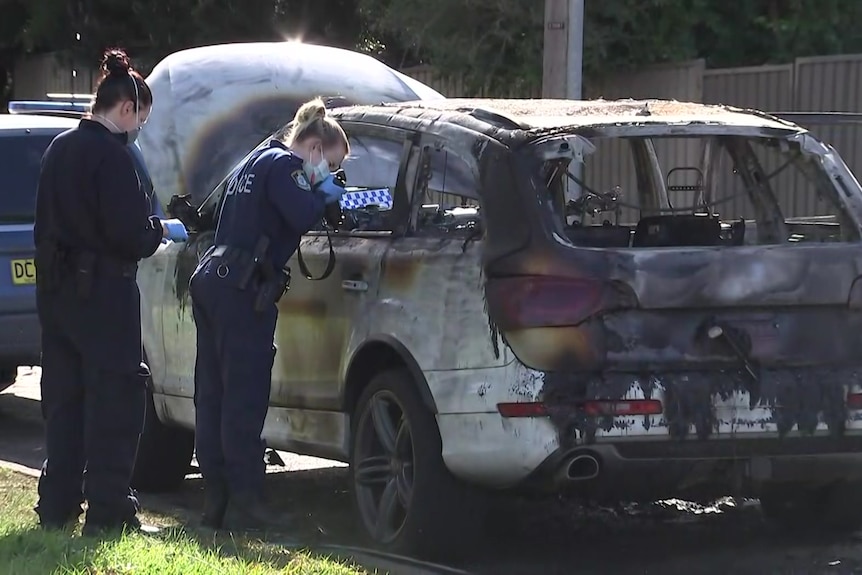 Forensic police officers take photographs of a burnt-out car. 